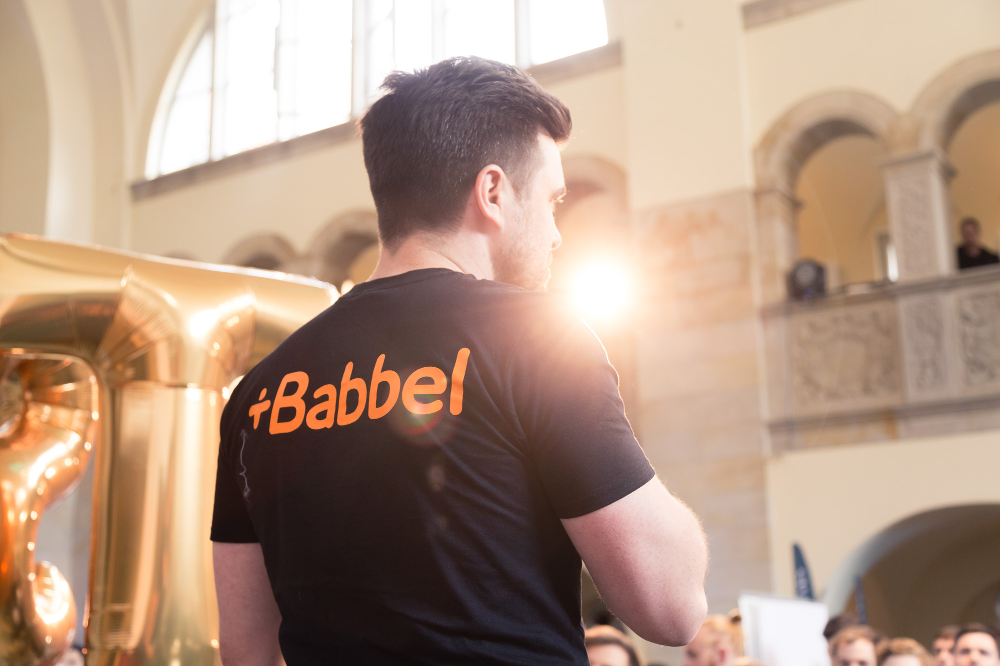 Presenter von hinten mit Lensflare und Babbel-Schriftzug auf dem Rücken